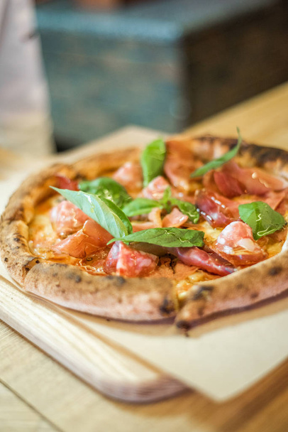 leckere Pizza steht auf dem Tisch, Pizza mit roter Sauce, Pancetta und Basilikum, italienische Küche, Pizzeria - Foto, Bild