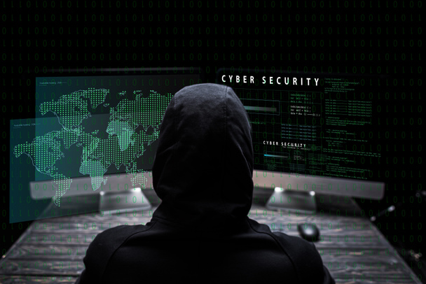 vista posterior del hacker encapuchado sentado cerca de monitores de computadora con letras de seguridad cibernética en negro
  - Foto, imagen
