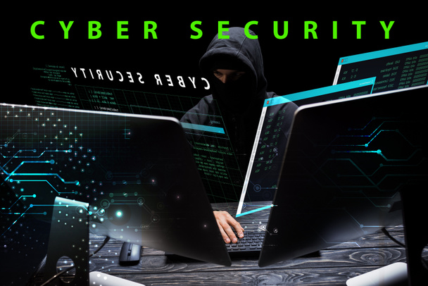 hacker in hood sitting near computer monitors near cyber security lettering on black  - Photo, Image