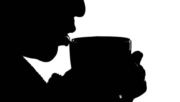 black silhouette of a girl on a white background who is drinking a hot drink from a mug - Фото, изображение
