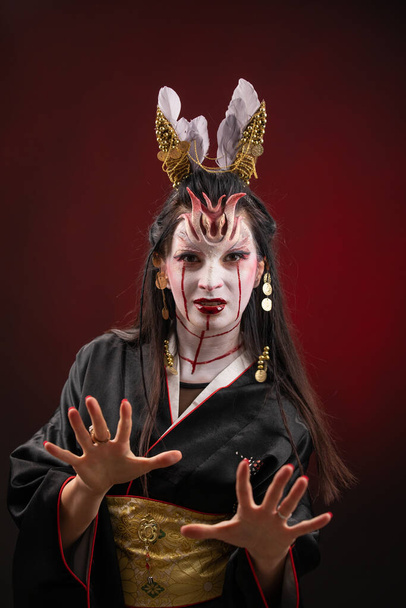 怖い魔女ゴーストストーリーの魔女アジアの女性は、口の血は黒い長い髪を巻き、スタジオの照明暗赤色の背景を見てください。ハロウィーンのために構成する - 写真・画像
