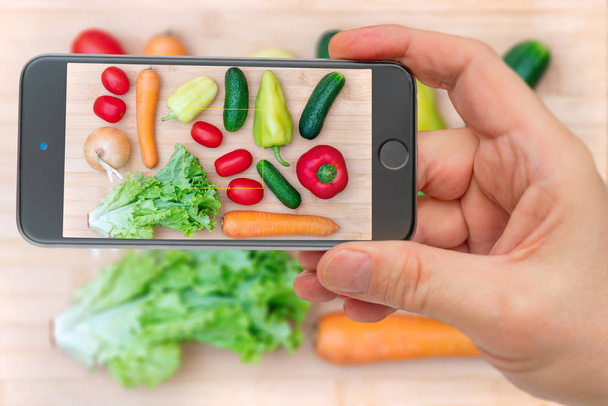 Vegetables on smartphone screen. Fresh vegetables on wooden cutting board. Set of vegetables for cooking healthy dishes. - Photo, Image