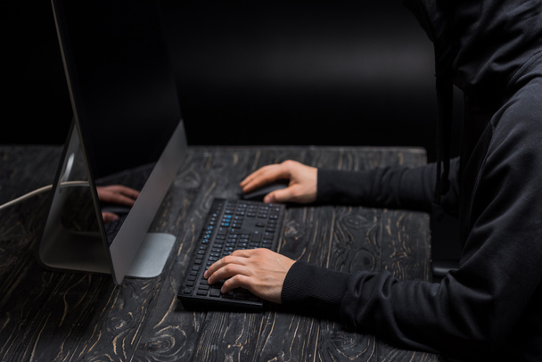 przycięty widok hakera wpisując na klawiaturze komputera na czarno  - Zdjęcie, obraz