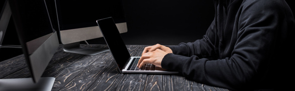panoramic shot of hacker typing on laptop keyboard isolated on black  - Photo, Image