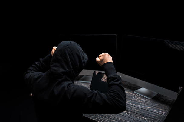 αναστατωμένος hacker με σφιγμένες γροθιές κοντά οθόνες υπολογιστή με λευκή οθόνη απομονώνονται σε μαύρο  - Φωτογραφία, εικόνα