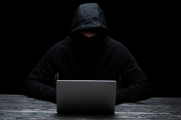hacker in hood using laptop isolated on black  - Photo, Image