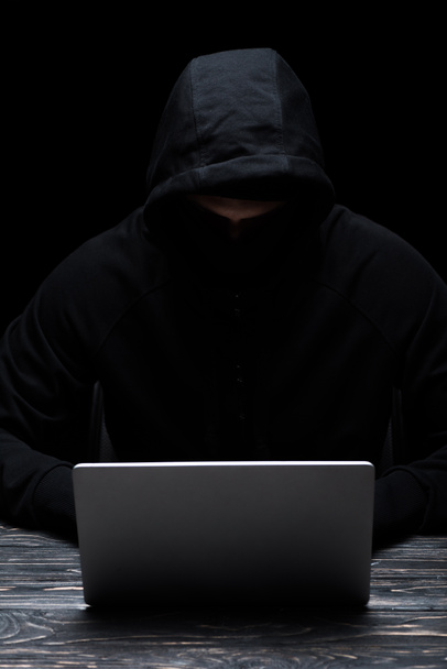 hacker anónimo en el capó usando el ordenador portátil aislado en negro
  - Foto, Imagen