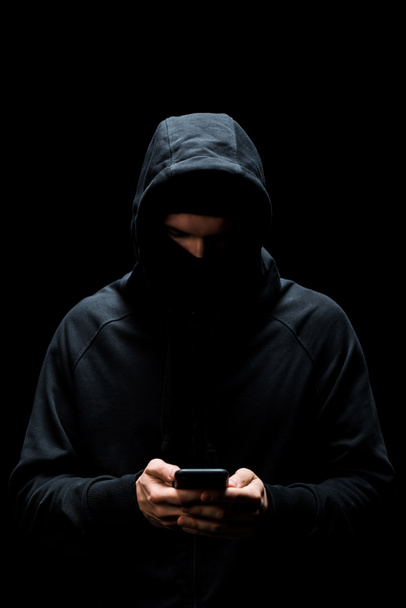 hacker en la capucha usando teléfono inteligente aislado en negro
  - Foto, Imagen