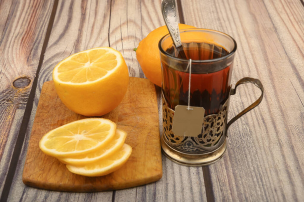 Čaj v fasetované sklenici ve vinobraní pohár držák, krájený citron na desce na dřevěném pozadí. Zavřít. - Fotografie, Obrázek
