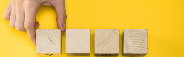 panoramic shot  man holding wooden cube isolated on yellow  - 写真・画像