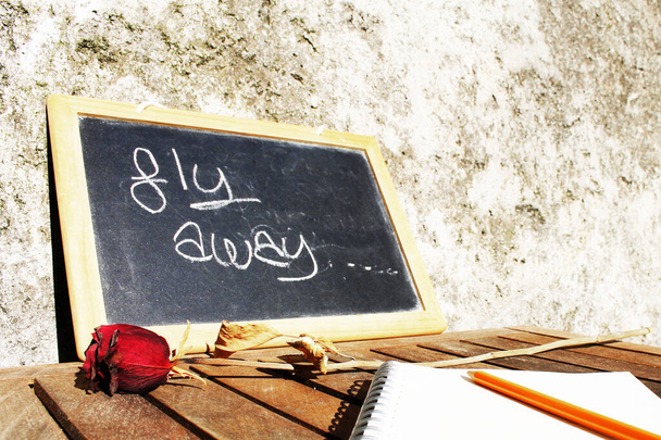 Chalkboard com o lema "voar para longe", com rosa vermelha seca
 - Foto, Imagem