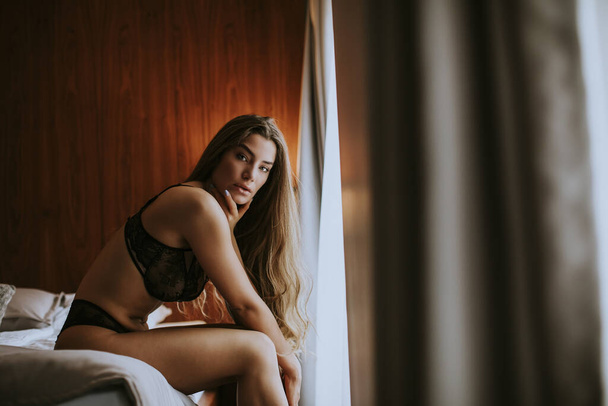 Γοητευτική σέξι νεαρή γυναίκα με εσώρουχα ξαπλωμένη στο κρεβάτι στο δωμάτιο - Φωτογραφία, εικόνα