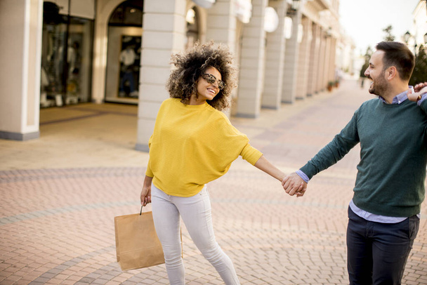 Hermosa joven pareja multiétnica con bolsas de papel disfrutando en las compras y divirtiéndose en la ciudad
 - Foto, imagen