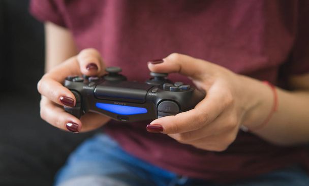 Ukraine, Odessa  July 2, 2019: A girl plays a video game on a playstation 4 joystick. The ps4 gamepad is in the girls hands. Gamer girl. - Photo, Image