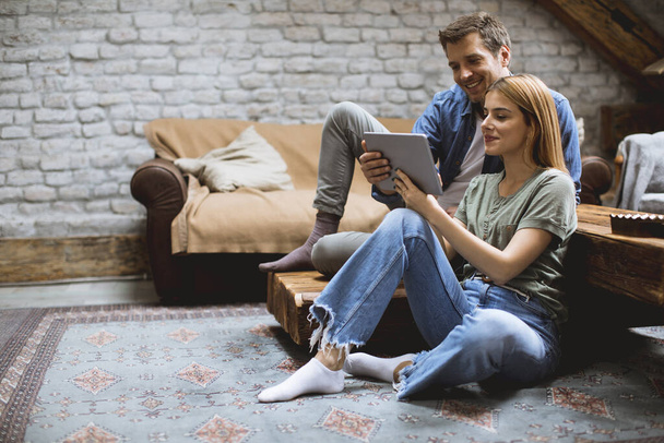 Щаслива пара, використовуючи цифровий планшет, сидячи разом о підлога в кімнаті
 - Фото, зображення