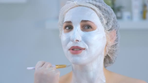 Cosmetologist is applying facial moisturizing mask on woman face using brush. - Felvétel, videó