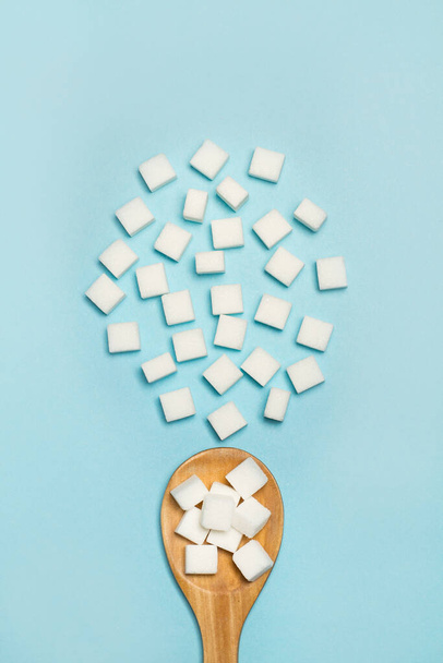 Valkoinen sokeri kuutiot puinen lusikka ja sininen tausta ylhäältä katsottuna
 - Valokuva, kuva