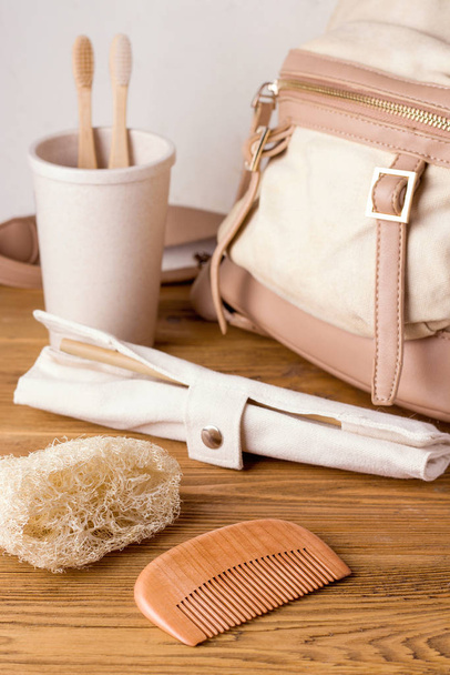 ecological accessories for bathroom and kitchen next to the backpack. in the foreground is a comb of wood and a washcloth of loofah. travel zero waste concept - Photo, image
