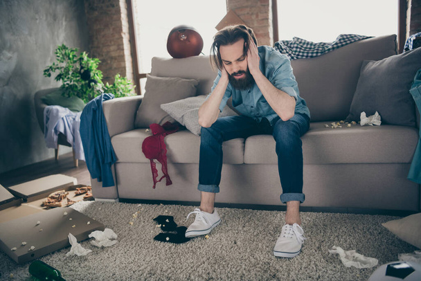 Photo of hipster crazy guy sitting sofa holding head intoxicated food underwear lying floor had stag party suffer hangover morning headache messy flat indoors - Фото, зображення