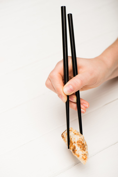 oříznutý pohled na ženu jíst lahodné gyoza s hůlkami na bílém dřevěném stole - Fotografie, Obrázek