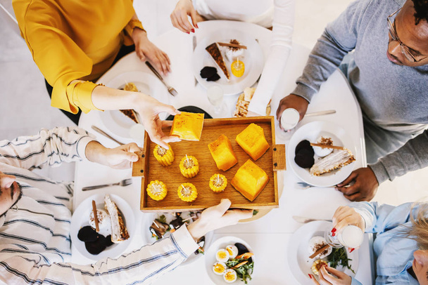 Blick von oben auf fünf multikulturelle Freunde, die am Esstisch sitzen und ein gesundes Mittagessen essen. - Foto, Bild