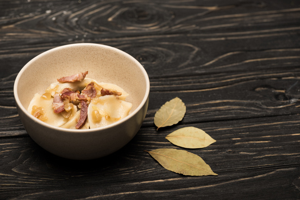 delicious varenyky with cracklings in bowl near bay leaves on black wooden table - 写真・画像