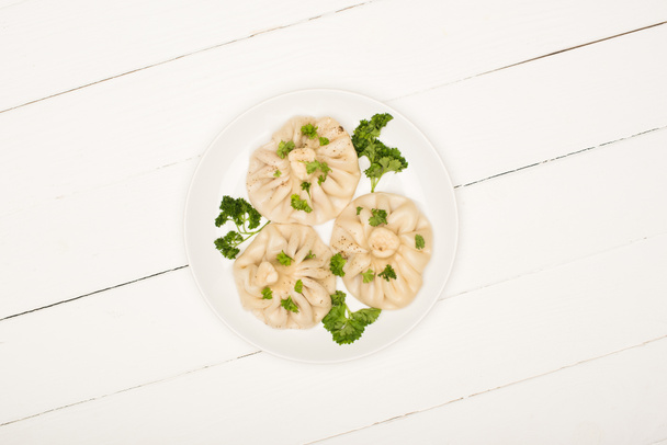 top view of delicious Khinkali with cilantro on plate on white wooden table - Fotó, kép