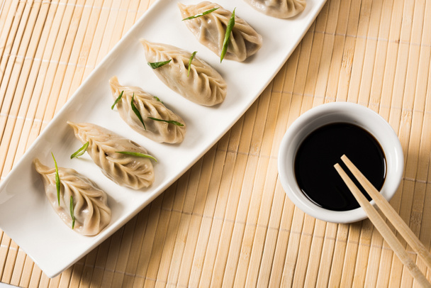 vista dall'alto di deliziosi gnocchi cinesi bolliti sul piatto vicino a bacchette e salsa di soia su tappetino di bambù
 - Foto, immagini
