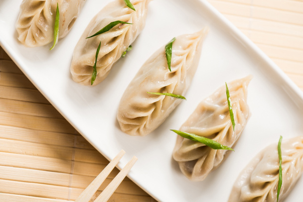 top view of delicious Chinese boiled dumplings on plate near chopsticks on bamboo mat - 写真・画像