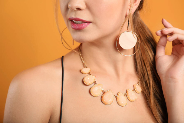 Jonge vrouw met mooie sieraden op kleur achtergrond, close-up - Foto, afbeelding