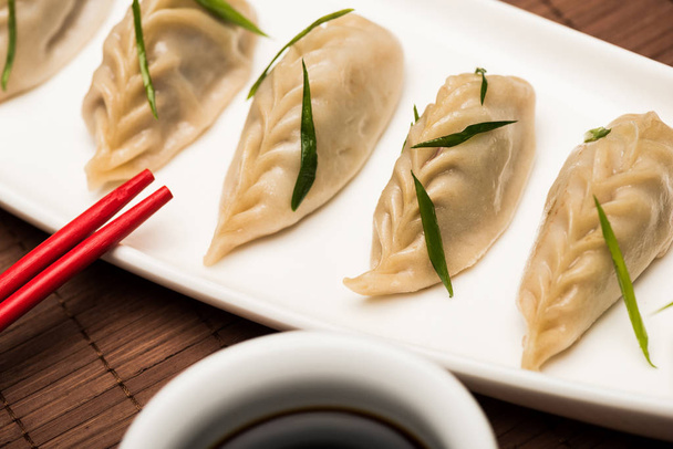 close up view of delicious Chinese boiled dumplings on plate near chopsticks and soy sauce on bamboo mat - Zdjęcie, obraz