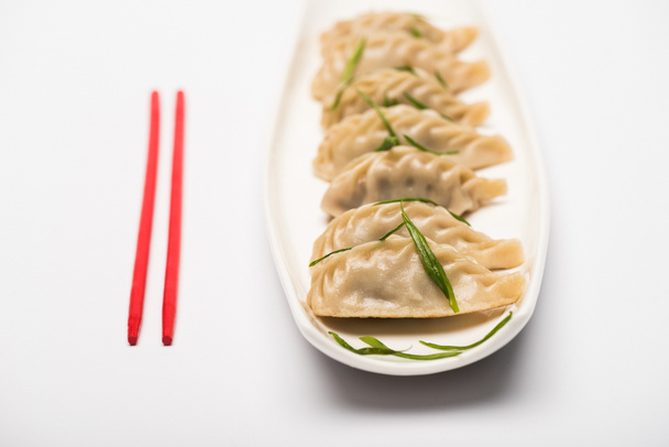 heerlijke Chinees gekookte knoedels op plaat in de buurt van eetstokjes op witte achtergrond - Foto, afbeelding