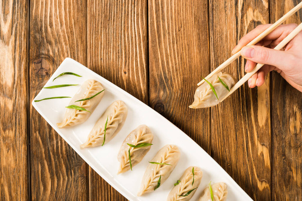 kivágott kilátás nő eszik finom kínai főtt gombóc evőpálcikával a fa asztalnál - Fotó, kép