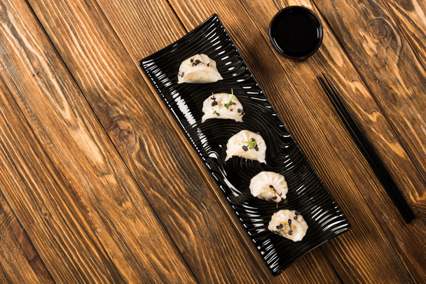 top view of delicious Chinese boiled dumplings on plate near chopsticks and soy sauce on wooden table - Fotoğraf, Görsel