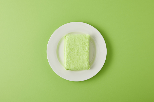 top view of white plate and sponge for dish washing on green - Photo, Image
