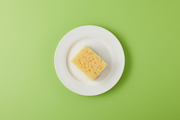 top view of plate and yellow sponge for dish washing on green - Foto, afbeelding