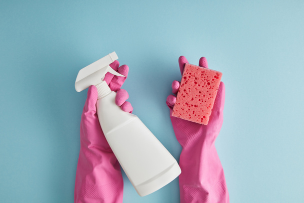 Ausgeschnittene Ansicht einer Haushälterin in rosa Gummihandschuhen mit Schwamm und Sprühflasche auf blauem Grund - Foto, Bild