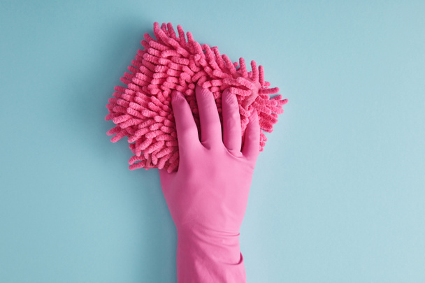 abgeschnittene Ansicht einer Haushälterin im Gummihandschuh mit rosa Lappen auf blau  - Foto, Bild