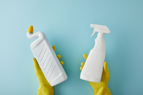 cropped view of housekeeper in rubber gloves holding spray bottle and bottle with toilet cleaner on blue - Photo, Image