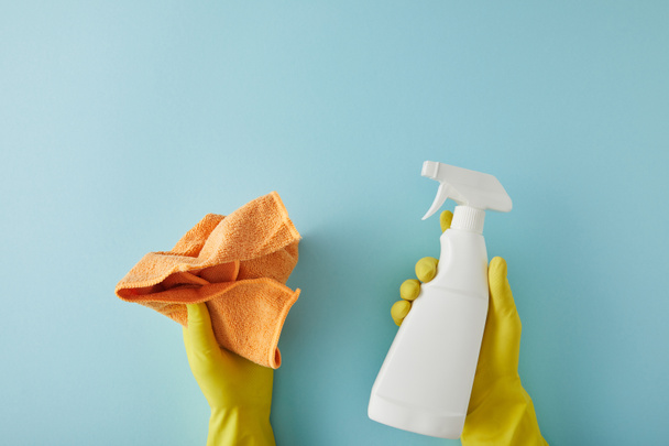 cropped view of housekeeper in yellow rubber gloves holding spray bottle and rag on blue - Фото, зображення