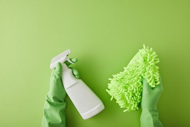 Top view of housekeeper in rubber gloves holding spray bottle and rag on green
  - Фото, изображение