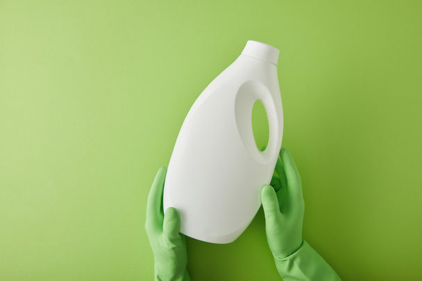 κορυφαία άποψη της οικονόμου σε γάντια από καουτσούκ κρατώντας μπουκάλι με προϊόν καθαρισμού σε πράσινο  - Φωτογραφία, εικόνα