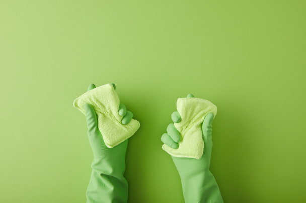 καλλιεργημένη άποψη της οικονόμου σε λαστιχένια γάντια κρατώντας δύο σφουγγάρια σε πράσινο  - Φωτογραφία, εικόνα