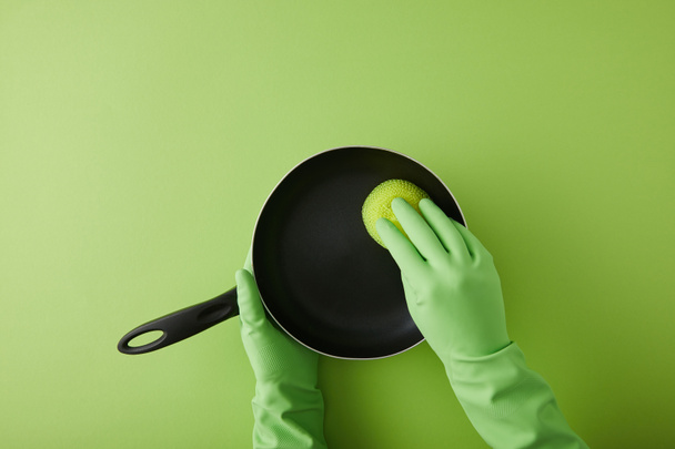 緑のスポンジでフライパンを洗うゴム手袋の家政婦のクロップドビュー  - 写真・画像