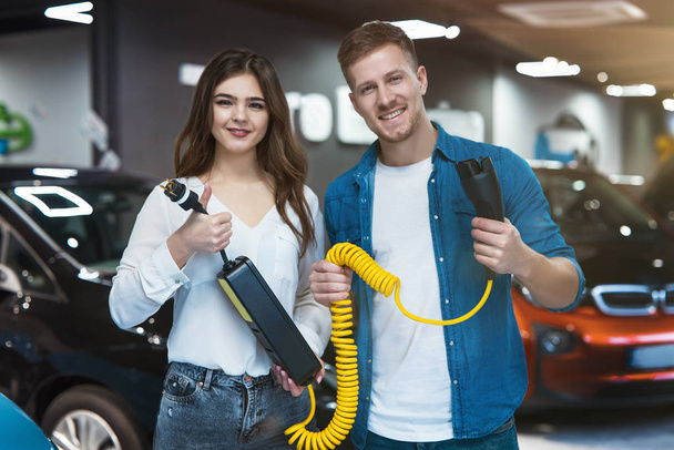 young family couple handsome man and beautiful brunette woman holding charging cable for electric car , looking satisfied - Foto, Imagem