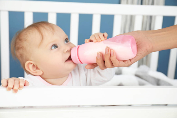 Äiti ruokkii vauvaa maidolla pullosta makuuhuoneessa
 - Valokuva, kuva