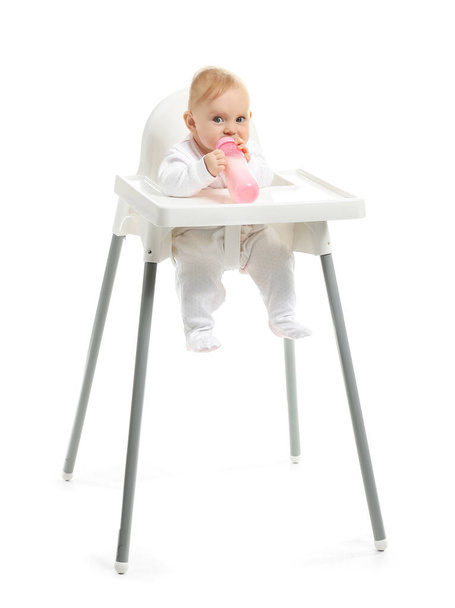 Bebé con biberón de leche sentado en trona sobre fondo blanco
 - Foto, Imagen