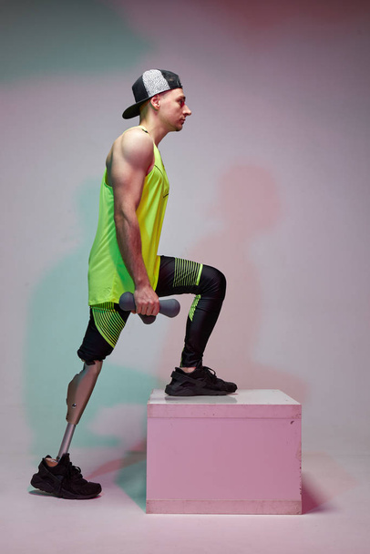 A young handsome man with a disability with a prosthetic leg is training in a gym with dumbbells. Fitness clothing. - Foto, imagen
