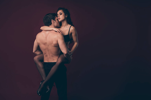 Rear view photo of two horny people handsome topless husband hold hands raise nude hot black boudoir wife smell kiss perfect body strong arms isolated maroon color background - Photo, Image