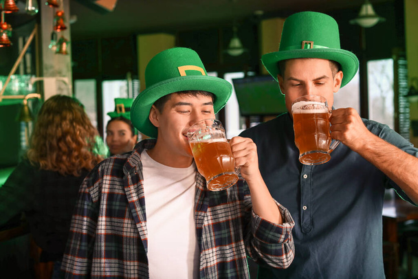 Young friends with beer celebrating St. Patrick's Day in pub - Фото, изображение